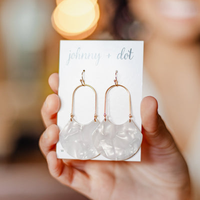 Sparkly white and gorgeous, our Birdie Earring is an open oval drop hoop that is sure to stun. With its geometric feel and white marbled shiny finish shown featured on an earring card,
