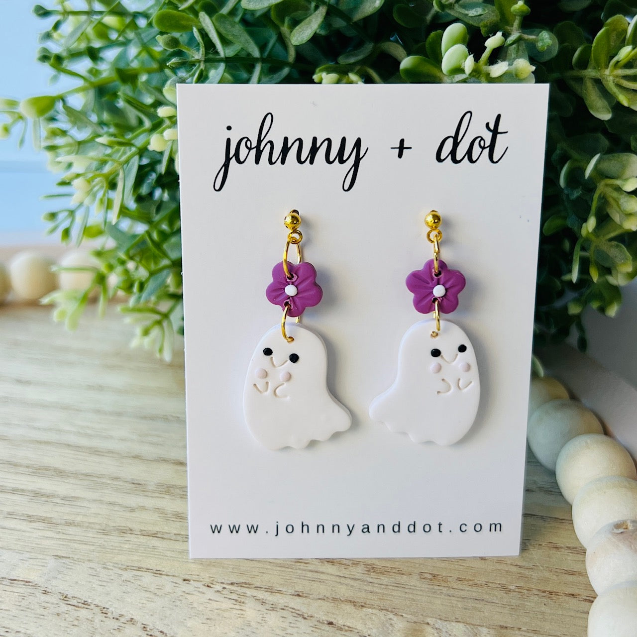Pair of ghost-shaped earrings with purple flowers on a 'johnny + dot' branded card.