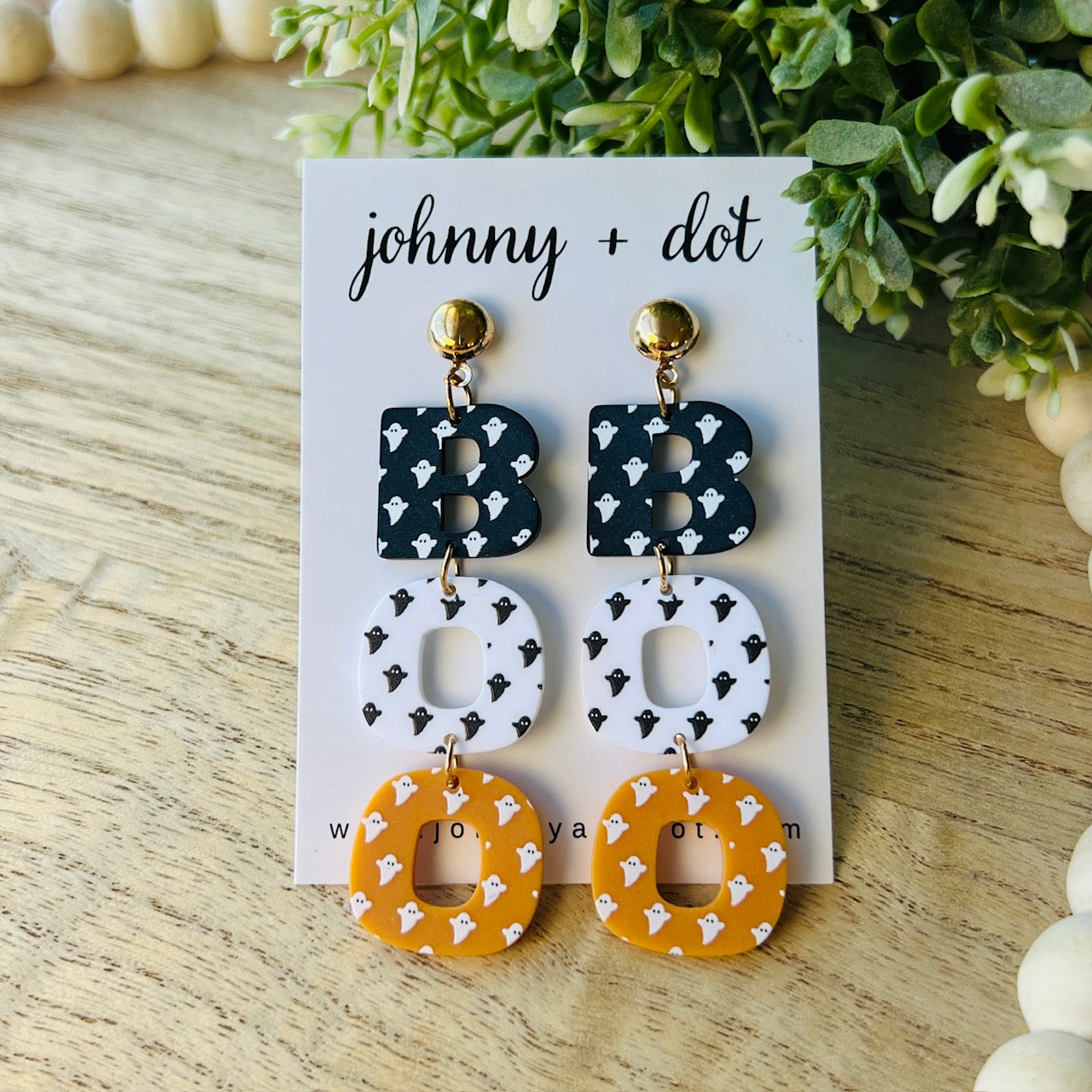 Pair of earrings on a 'johnny + dot' branded card with greenery in the background.