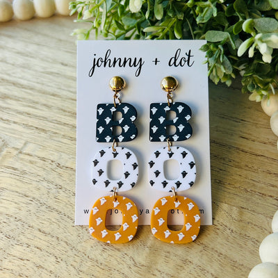 Pair of earrings on a 'johnny + dot' branded card with greenery in the background.