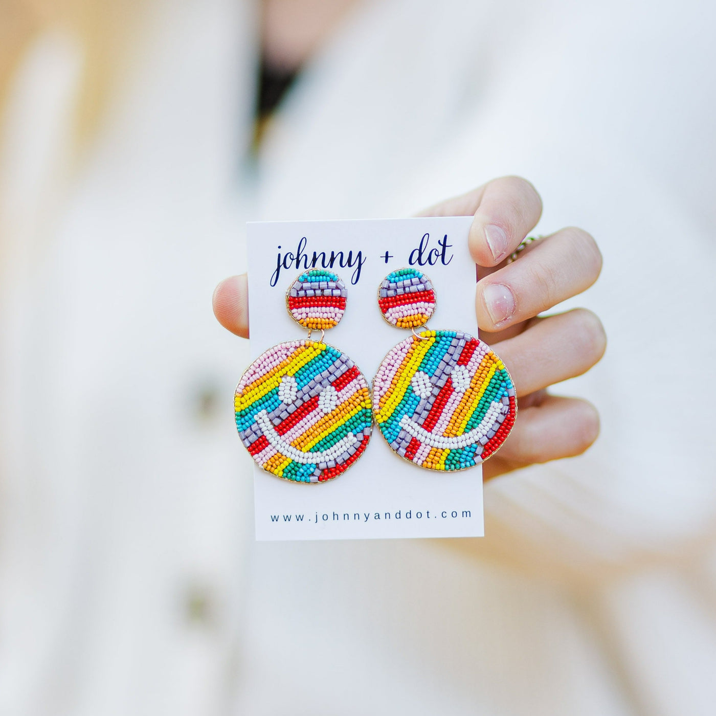 Model holding multicolored rainbow beaded happy face teacher earrings.