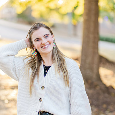 Model wearing multicolored rainbow beaded happy face teacher earrings.