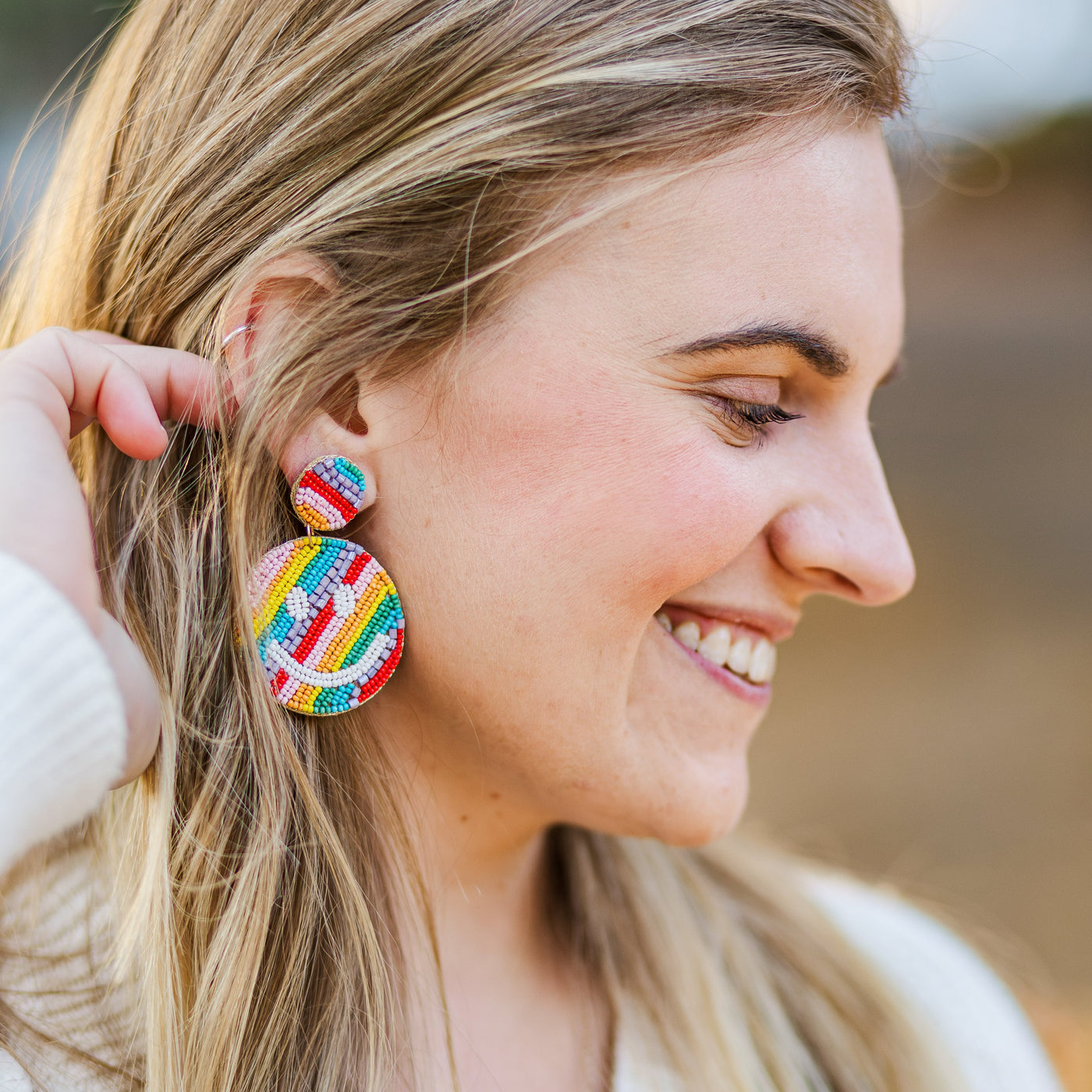 Model wearing multicolored rainbow beaded happy face teacher earrings.