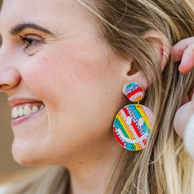Model wearing multicolored rainbow beaded happy face teacher earrings.