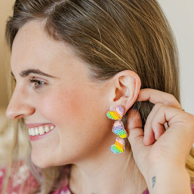 Model holding a pair of Beaded Pastel Heart Trio Dangle Earrings.