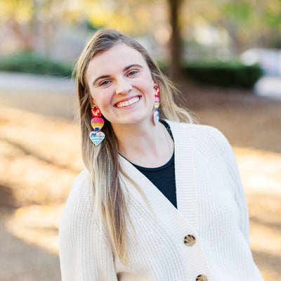 Model wearing a pair of large Beaded Teacher Earrings that include triple dangle of an apple, pencil, and A+ paper.