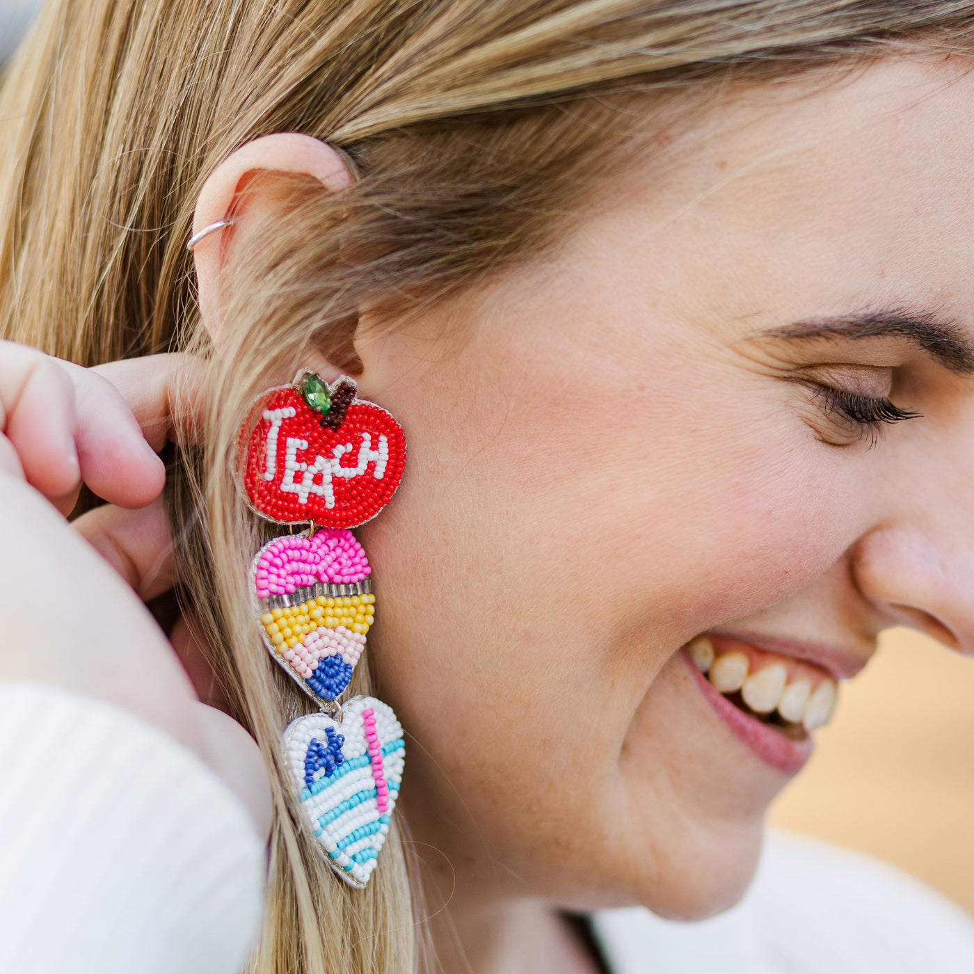 Model wearing a pair of large Beaded Teacher Earrings that include triple dangle of an apple, pencil, and A+ paper.