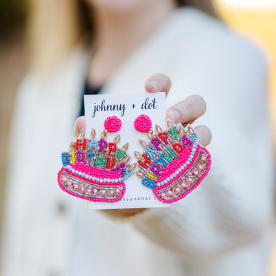 Model holding a pair of Large Beaded Happy Birthday Cake Earrings.