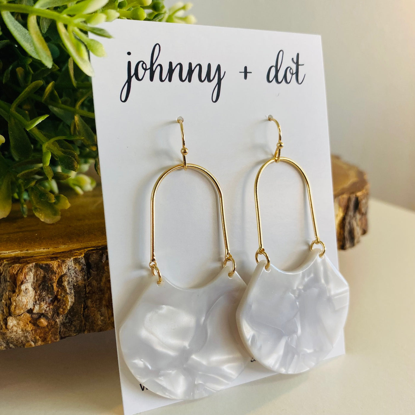 An open oval drop hoop earring with gold hardware and a white marble acetate finish displayed on a Johnny & Dot earring card.