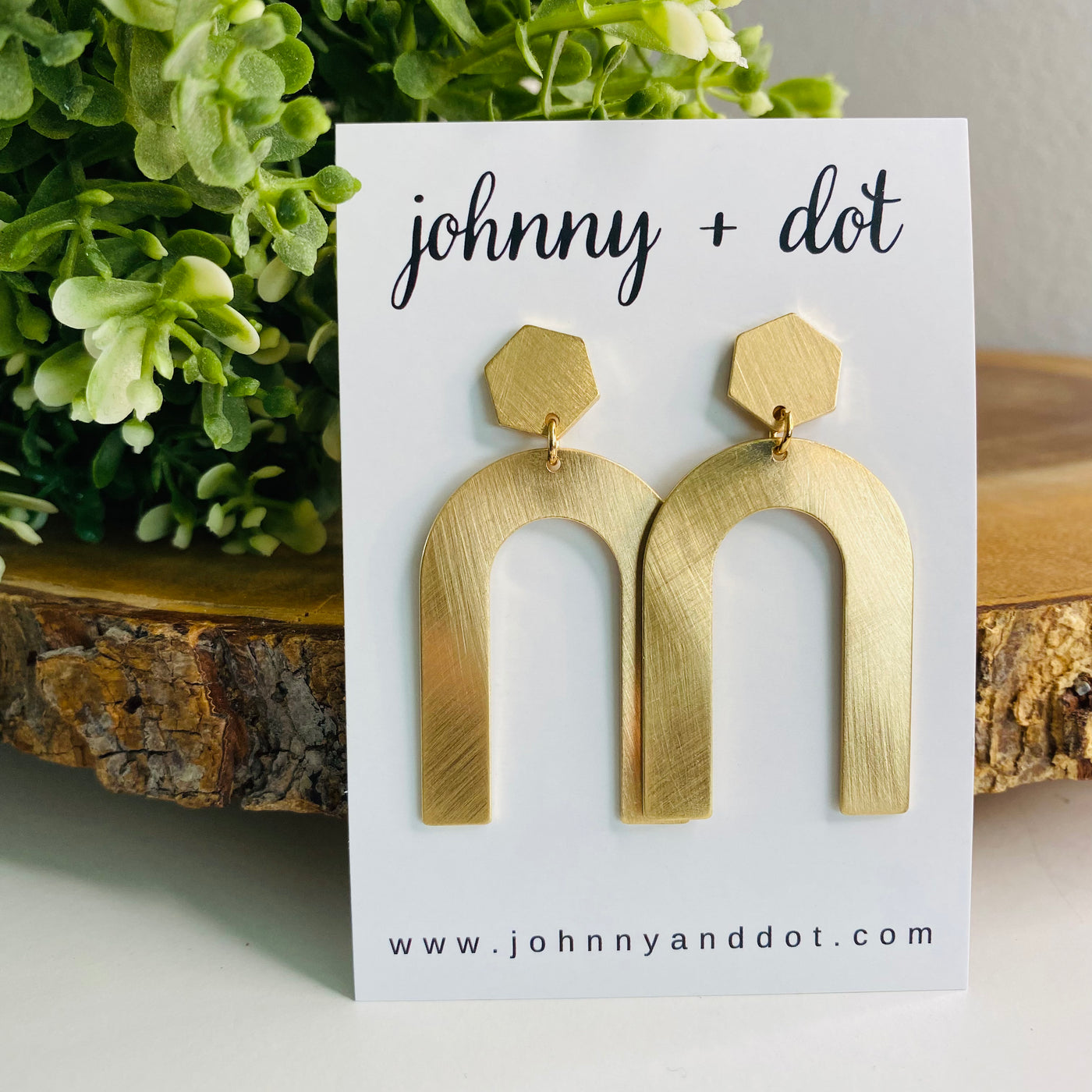 An upside u-shape metal earring with a gold metallic brushed sheen with a hexagon post-back design displayed on a Johnny & Dot Earring card. 